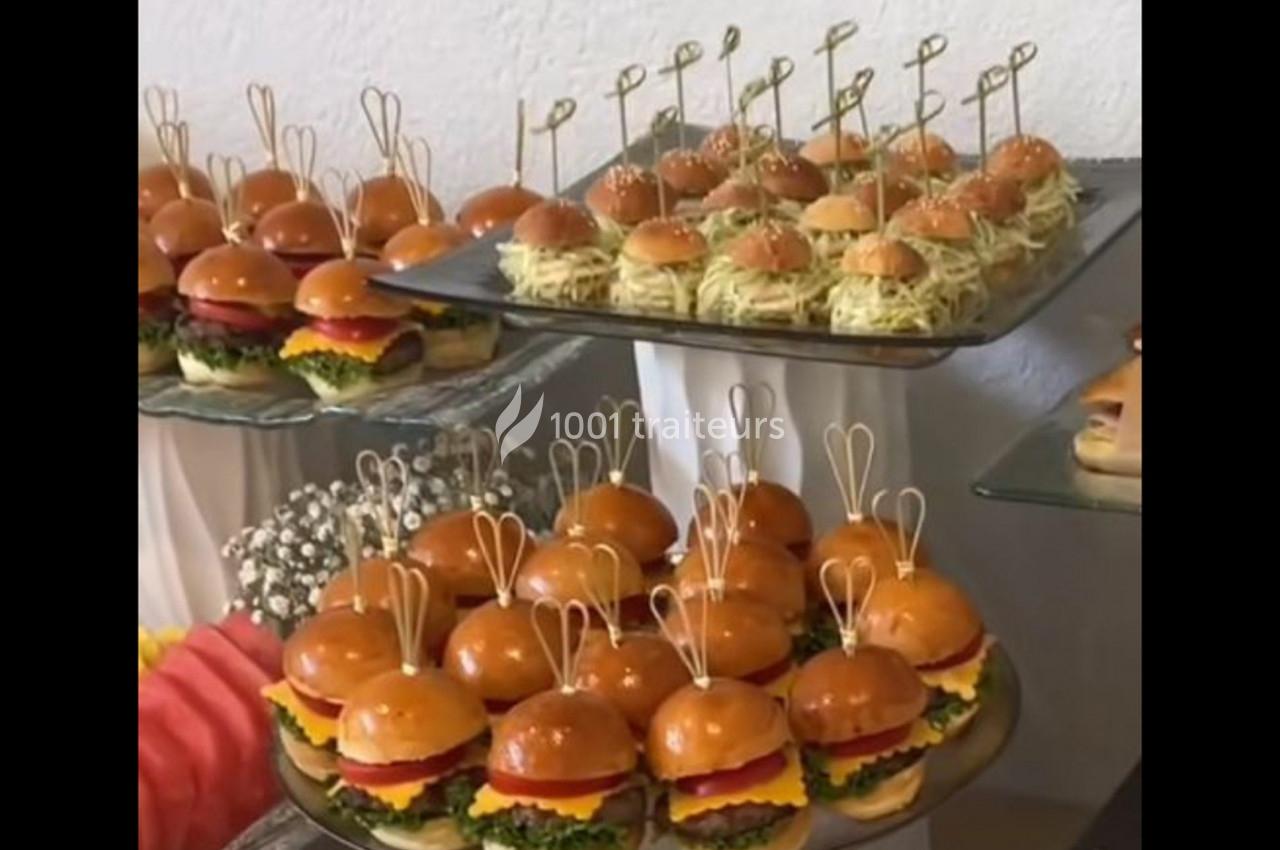 Plateaux de mini-burgers et bouchées apéritives présentés sur des supports en verre pour un buffet.