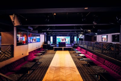 Intérieur d'une salle moderne avec mezzanine, éclairage tamisé, motifs géométriques au sol et écran lumineux au fond.