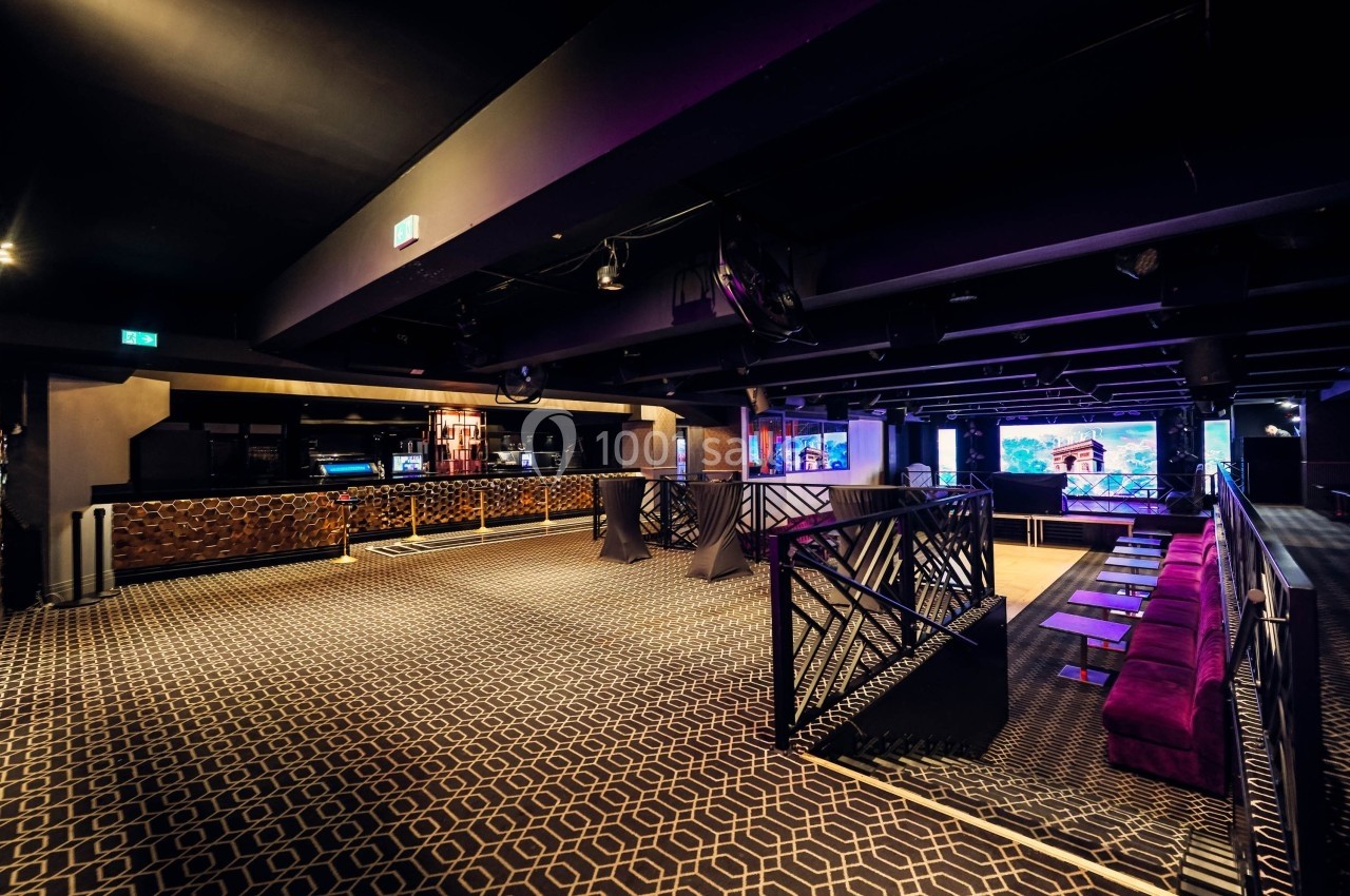 Salle de réception moderne avec éclairage tamisé, bar en fond, sièges violets et motifs géométriques au sol.