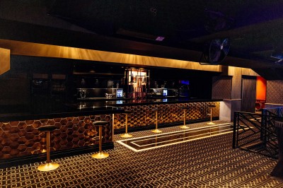 Intérieur d'une salle moderne avec mezzanine, éclairage tamisé, motifs géométriques au sol et écran lumineux au fond.