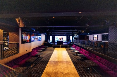 Intérieur d'une salle moderne avec mezzanine, éclairage tamisé, motifs géométriques au sol et écran lumineux au fond.
