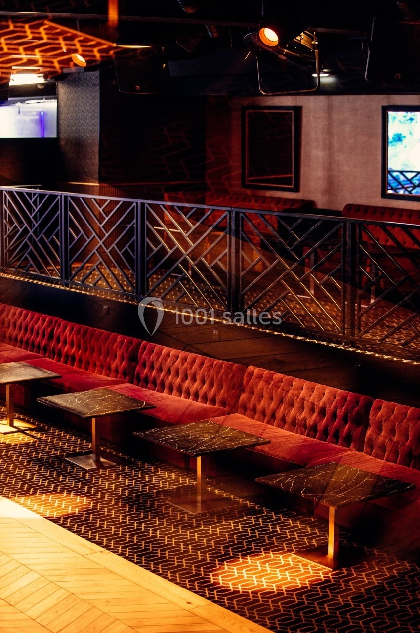 Banquettes rouges et tables en marbre noir dans un espace intérieur avec une balustrade décorative et un éclairage tamisé.