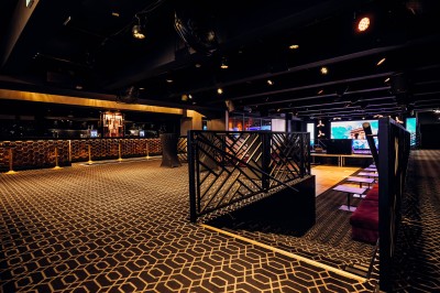 Intérieur d'une salle moderne avec mezzanine, éclairage tamisé, motifs géométriques au sol et écran lumineux au fond.