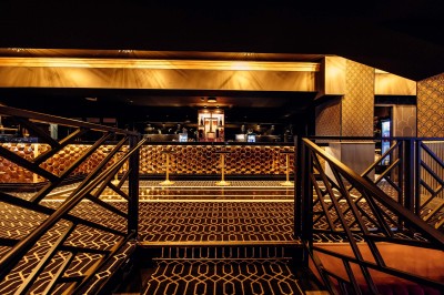 Intérieur d'une salle moderne avec mezzanine, éclairage tamisé, motifs géométriques au sol et écran lumineux au fond.