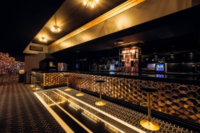 Intérieur d'une salle moderne avec mezzanine, éclairage tamisé, motifs géométriques au sol et écran lumineux au fond.