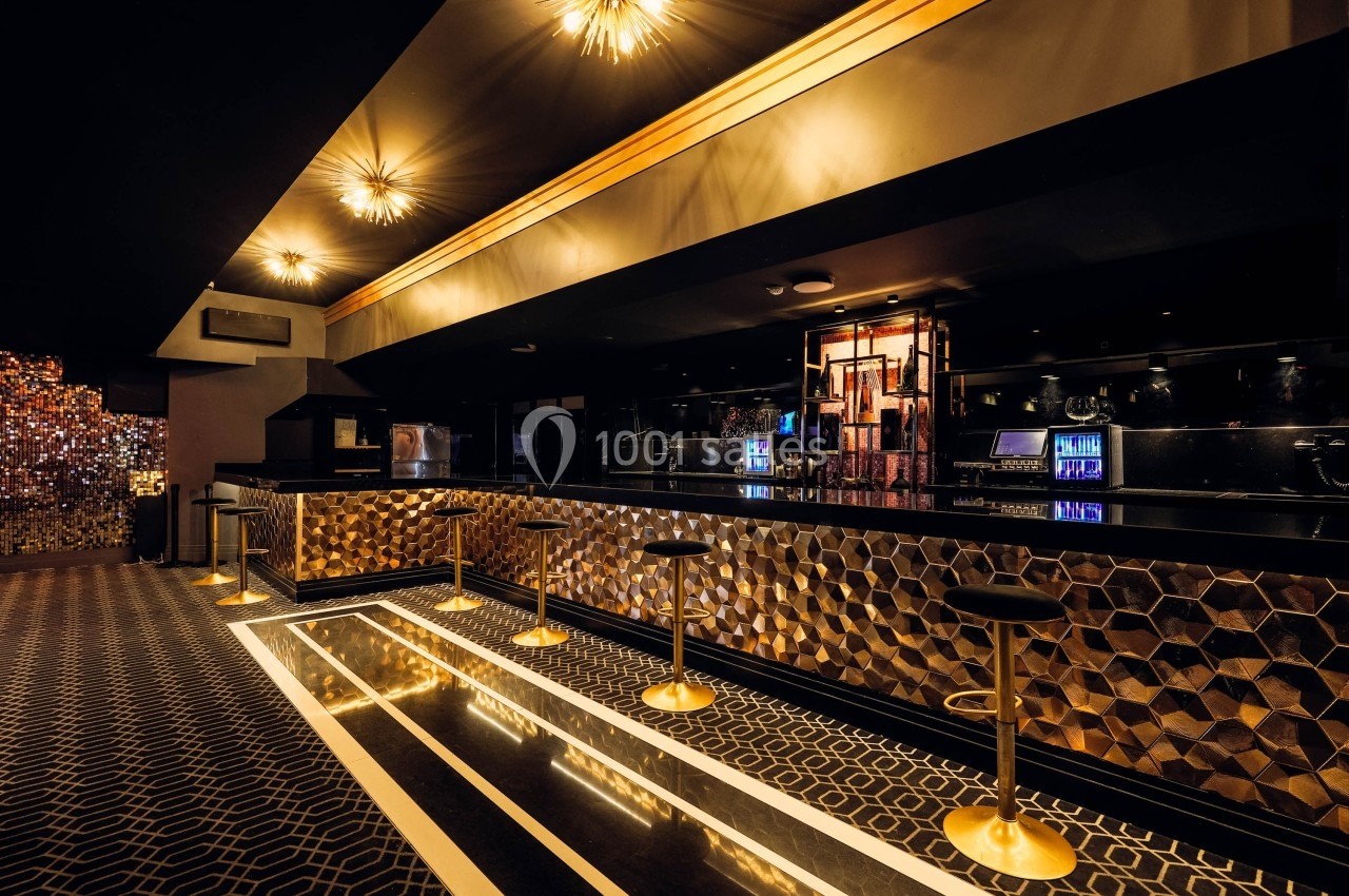 Intérieur d'un bar élégant avec comptoir doré, tabourets hauts et éclairage tamisé.