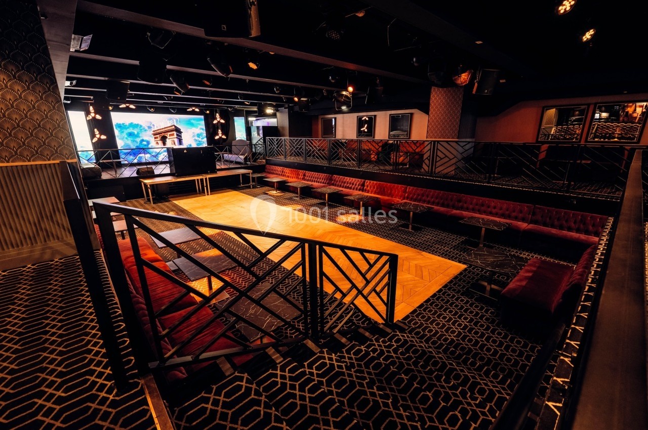 Salle de spectacle vide avec piste en bois, banquettes rouges et éclairage tamisé.
