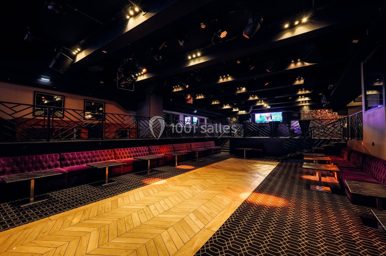 Salle vide avec parquet central, banquettes rouges sur les côtés et éclairage tamisé dans une ambiance de club.