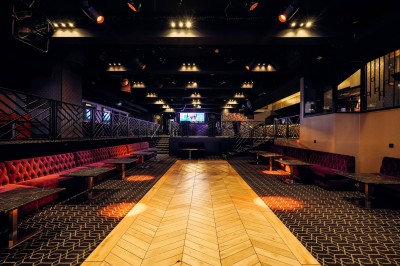 Intérieur d'une salle moderne avec mezzanine, éclairage tamisé, motifs géométriques au sol et écran lumineux au fond.