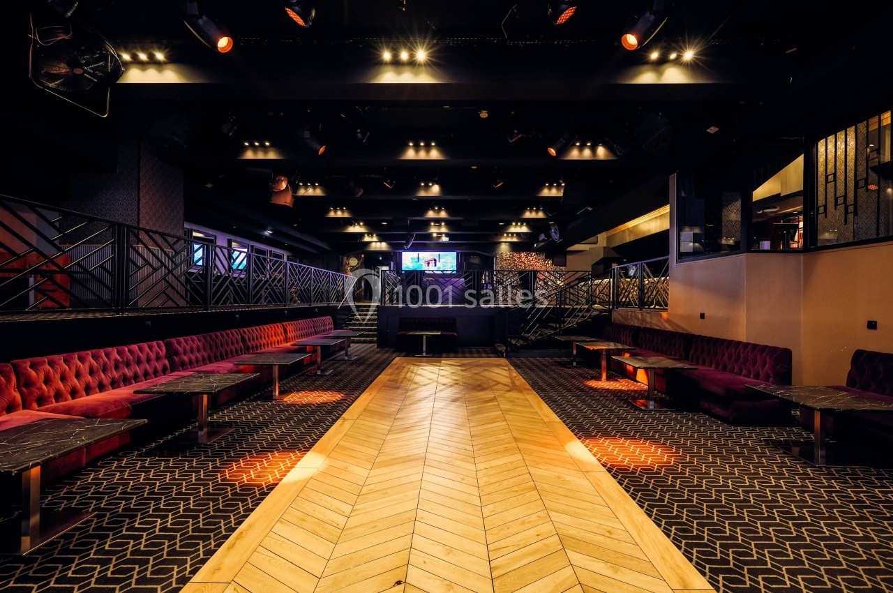 Salle de réception moderne avec banquettes rouges, tables en marbre et parquet clair, éclairée par des spots.