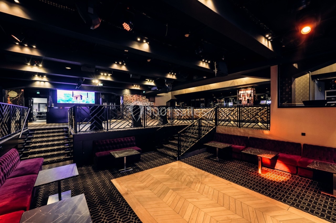 Salle moderne avec éclairage tamisé, banquettes rouges, tables basses et parquet au centre, ambiance lounge.