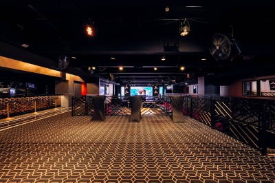 Intérieur d'une salle moderne avec mezzanine, éclairage tamisé, motifs géométriques au sol et écran lumineux au fond.