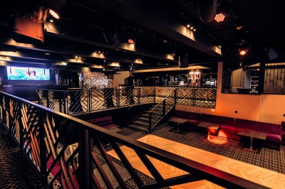 Intérieur d'une salle moderne avec mezzanine, éclairage tamisé, motifs géométriques au sol et écran lumineux au fond.