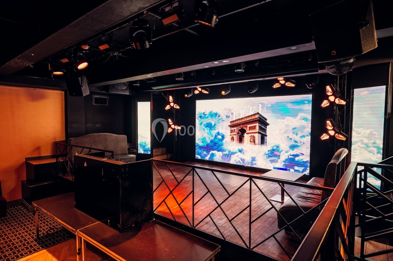 Scène intérieure avec écran géant affichant l'Arc de Triomphe, entourée de sièges et éclairée par des projecteurs.