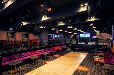 Intérieur d'une salle moderne avec mezzanine, éclairage tamisé, motifs géométriques au sol et écran lumineux au fond.