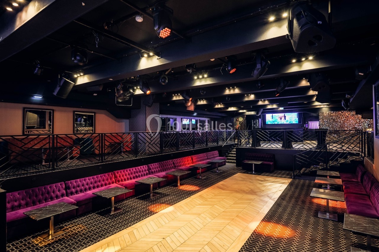 Salle de réception avec banquettes violettes, tables basses, parquet central et éclairage tamisé.