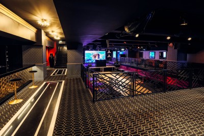Intérieur d'une salle moderne avec mezzanine, éclairage tamisé, motifs géométriques au sol et écran lumineux au fond.