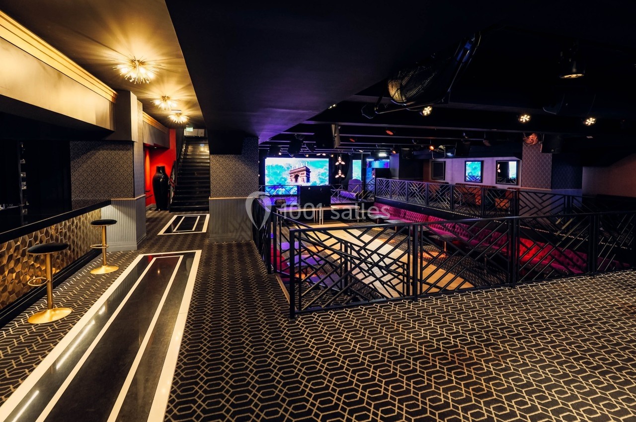 Intérieur d'une salle moderne avec mezzanine, éclairage tamisé, motifs géométriques au sol et écran lumineux au fond.