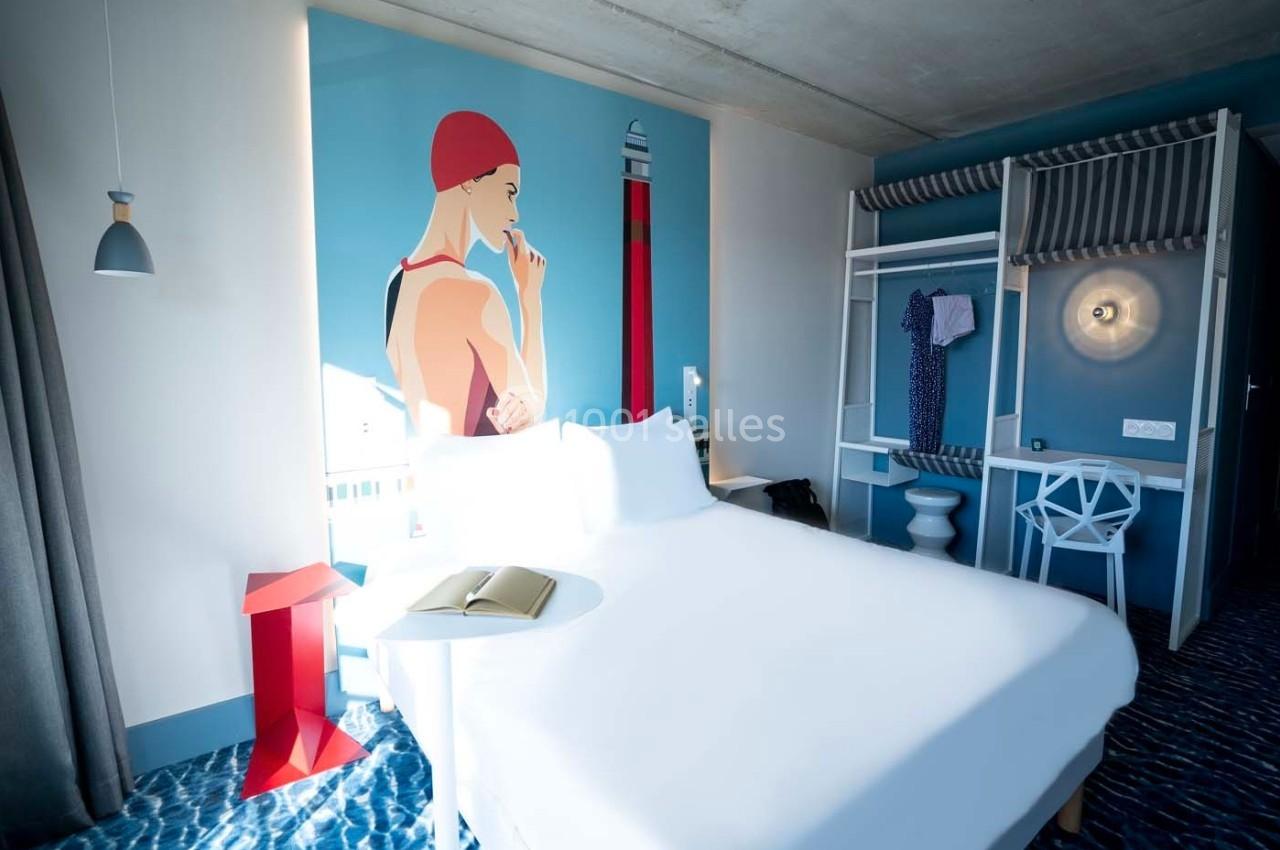 Chambre d'hôtel moderne avec lit double, décoration murale colorée, penderie ouverte et lumière naturelle.