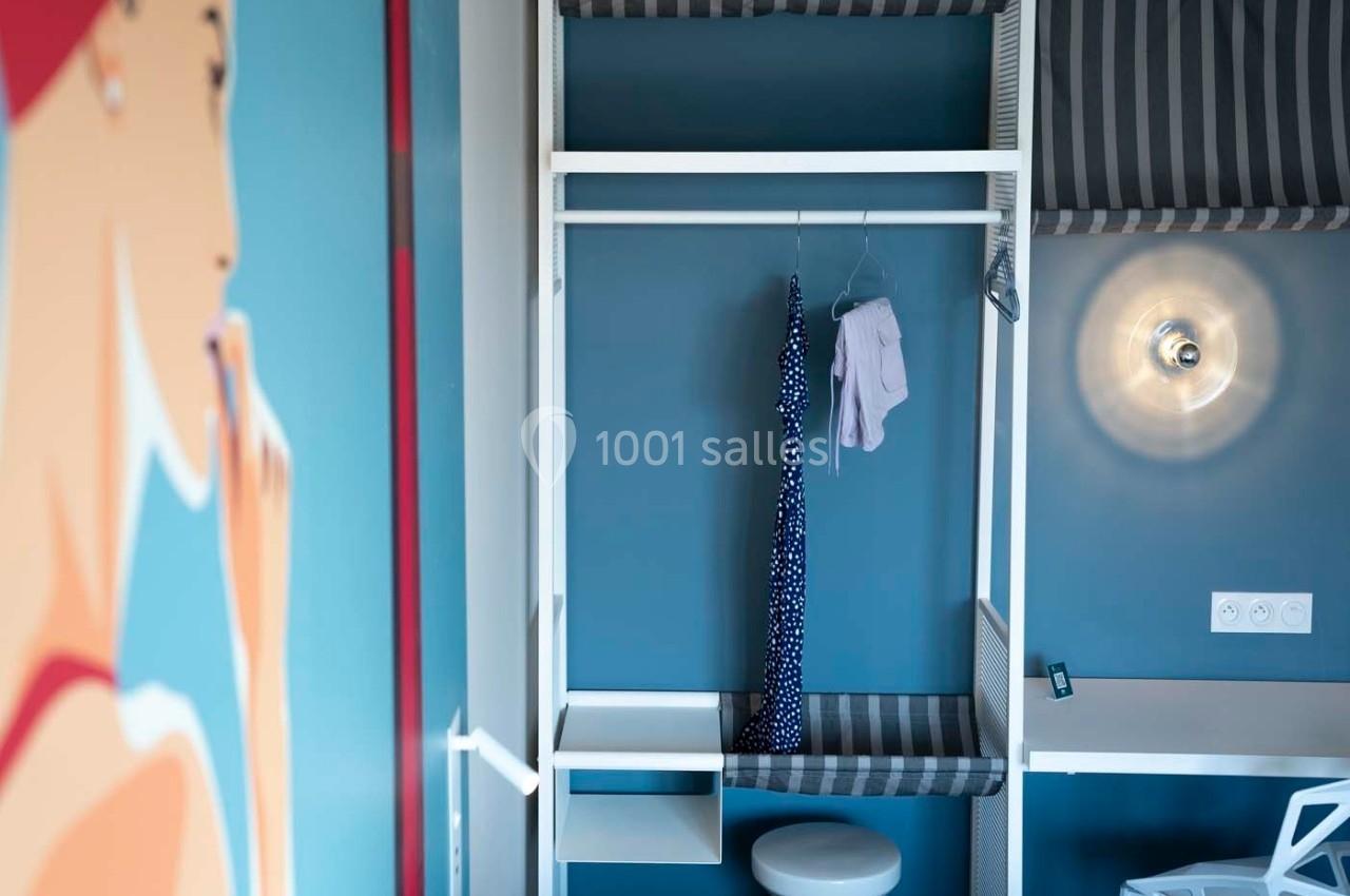 Intérieur d'une chambre avec un dressing ouvert, une robe suspendue, un bureau et une lampe murale allumée.