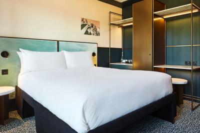 Lit avec tête de lit en velours, table d'appoint ronde et fenêtre avec rideaux dans une chambre lumineuse.