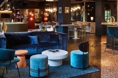 Lit avec tête de lit en velours, table d'appoint ronde et fenêtre avec rideaux dans une chambre lumineuse.