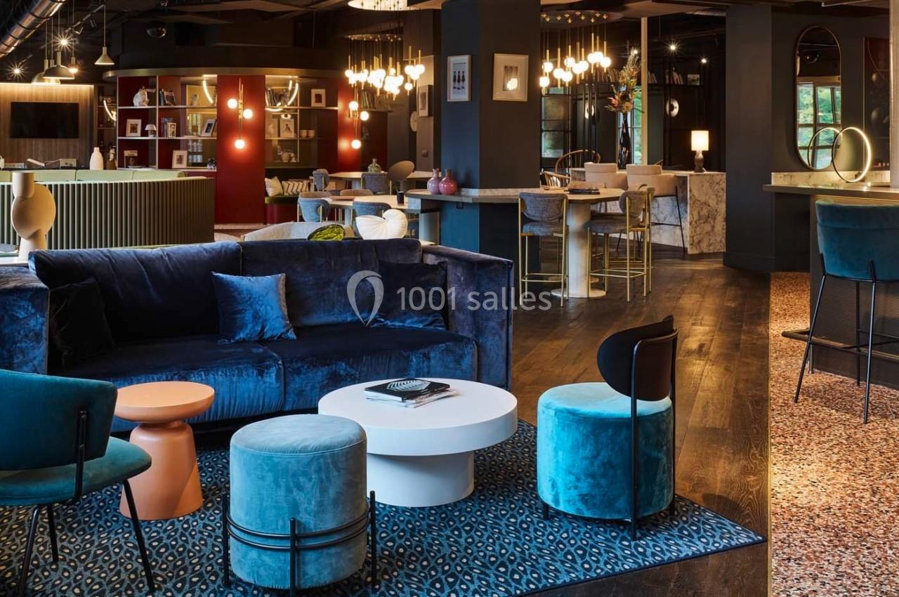 Espace intérieur moderne avec canapé bleu, tables basses, chaises design et éclairage chaleureux.