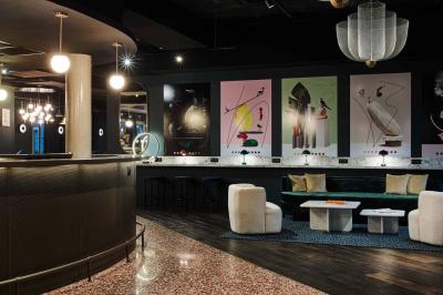 Lit avec tête de lit en velours, table d'appoint ronde et fenêtre avec rideaux dans une chambre lumineuse.