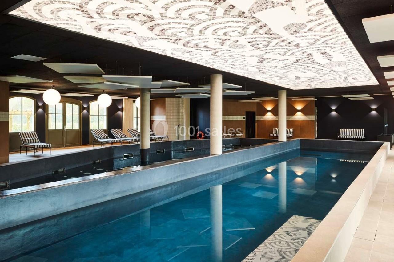 Piscine intérieure avec un plafond décoratif, entourée de chaises longues et d'un éclairage tamisé.