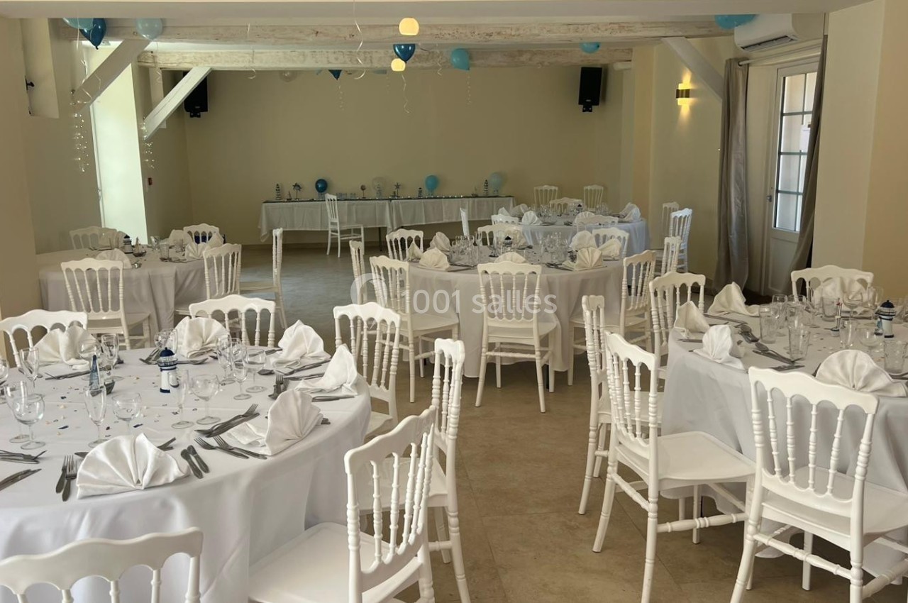 Salle de réception décorée avec des tables rondes dressées de nappes blanches, serviettes pliées et touches de bleu.