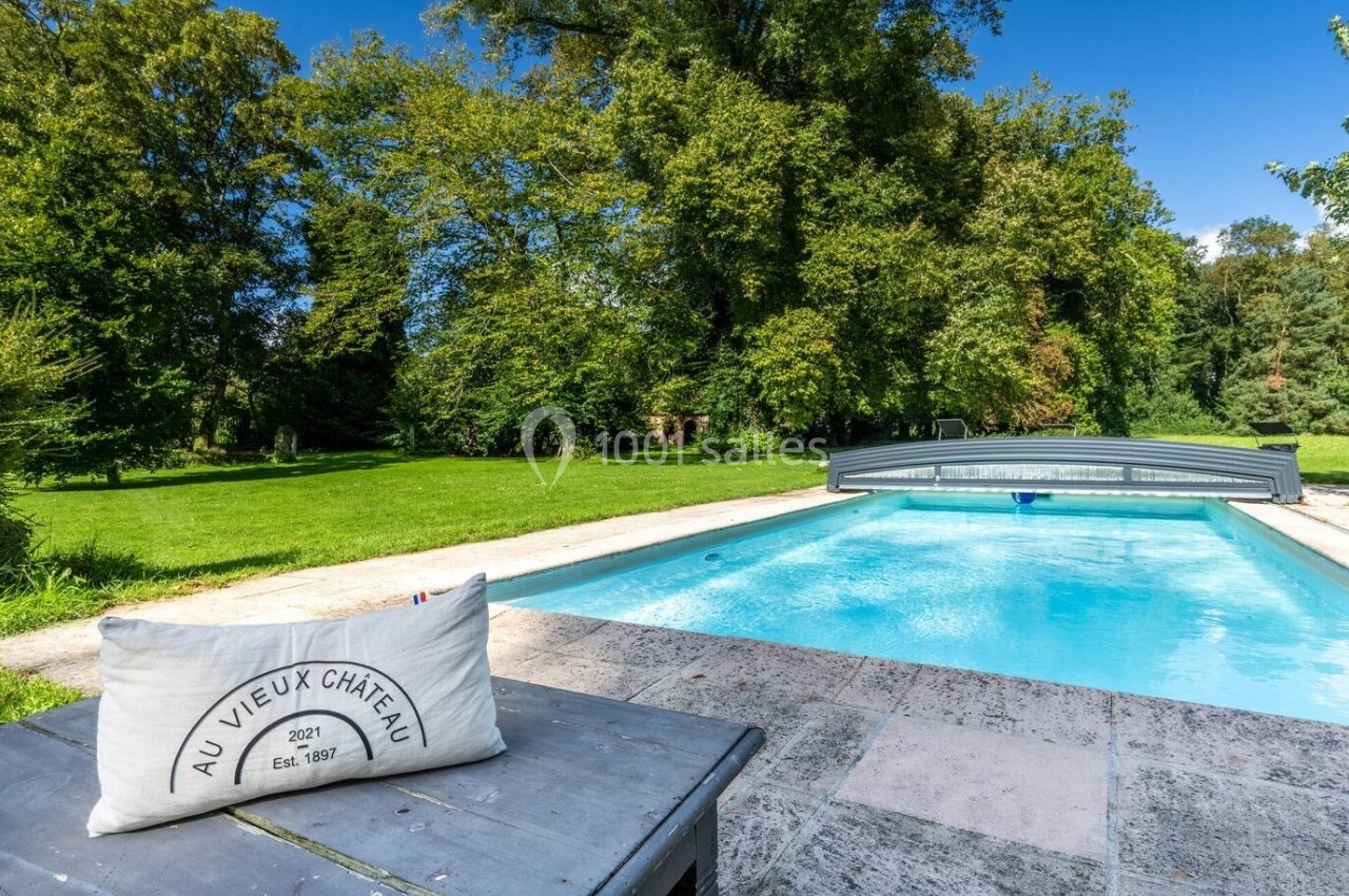 Piscine extérieure avec abri coulissant, entourée de verdure et d'arbres, vue depuis une table en pierre.