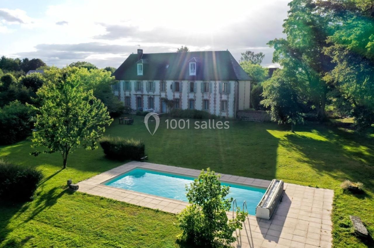 Manoir ancien entouré d'un grand jardin verdoyant avec une piscine rectangulaire au premier plan.