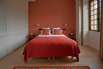 Salon lumineux avec murs terracotta, mobilier éclectique, grande fenêtre, tableau classique et étagère courbe.
