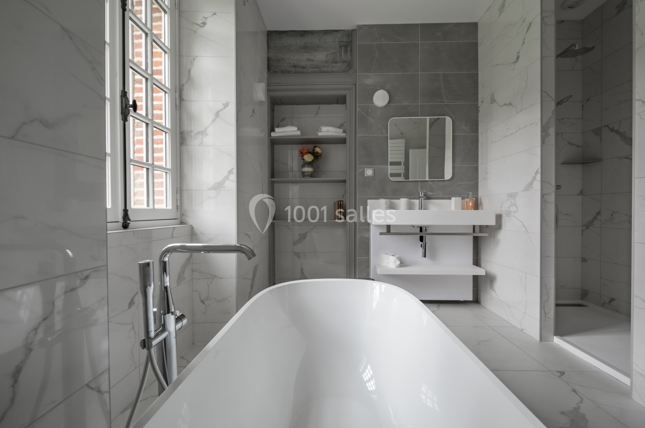 Salle de bain moderne avec baignoire, lavabo double, douche et étagères, décorée de carrelage effet marbre.