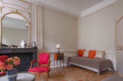 Salon lumineux avec murs terracotta, mobilier éclectique, grande fenêtre, tableau classique et étagère courbe.