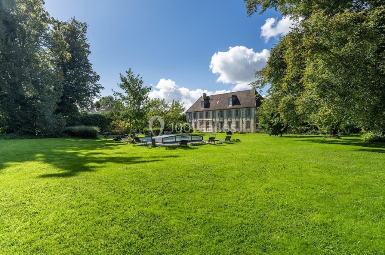 Grande maison en pierre entourée d'un vaste jardin verdoyant avec pelouse, arbres et mobilier d'extérieur.