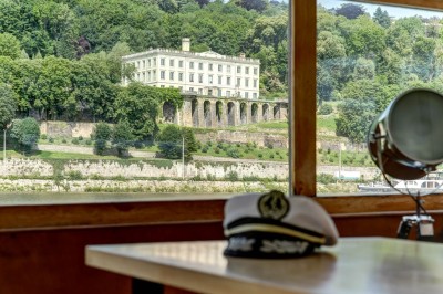 Bateau amarré sur un quai, avec vue sur une rivière, des bâtiments historiques et un pont en arrière-plan.