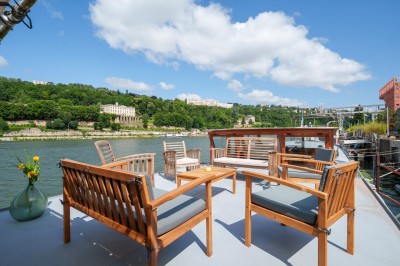 Bateau amarré sur un quai, avec vue sur une rivière, des bâtiments historiques et un pont en arrière-plan.