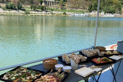 Bateau amarré sur un quai, avec vue sur une rivière, des bâtiments historiques et un pont en arrière-plan.