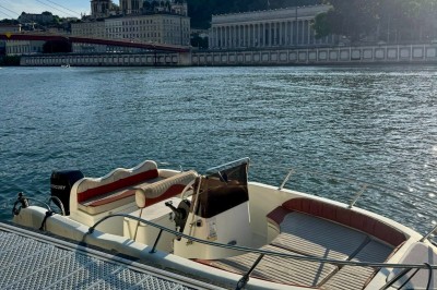 Bateau amarré sur un quai, avec vue sur une rivière, des bâtiments historiques et un pont en arrière-plan.