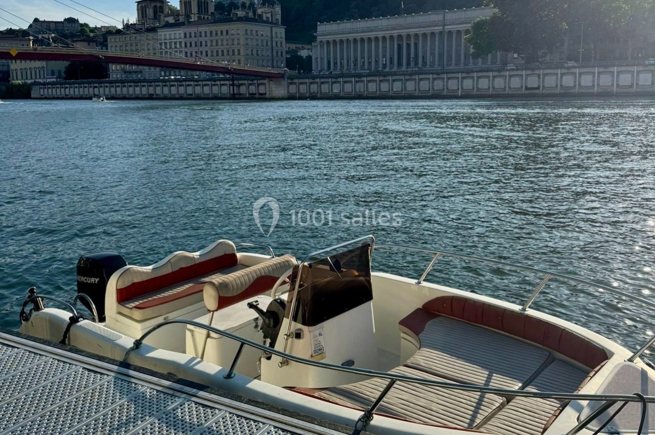 Bateau amarré sur un quai, avec vue sur une rivière, des bâtiments historiques et un pont en arrière-plan.