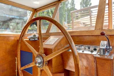 Poste de pilotage en bois d'un bateau avec un grand volant, des commandes et des fenêtres laissant entrer la lumière.