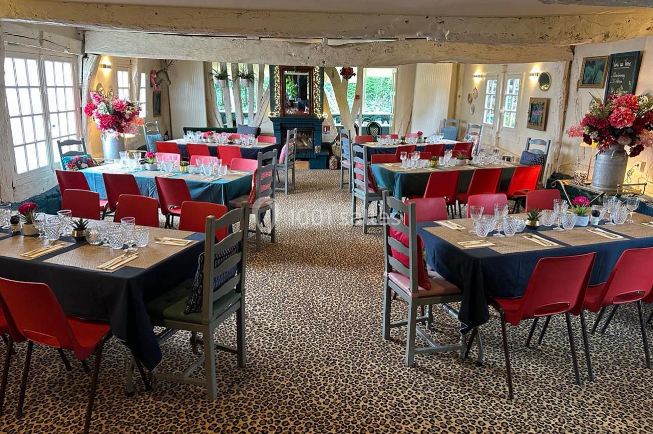 Salle de restaurant décorée avec des tables dressées, chaises colorées et fleurs, dans un cadre rustique avec poutres…