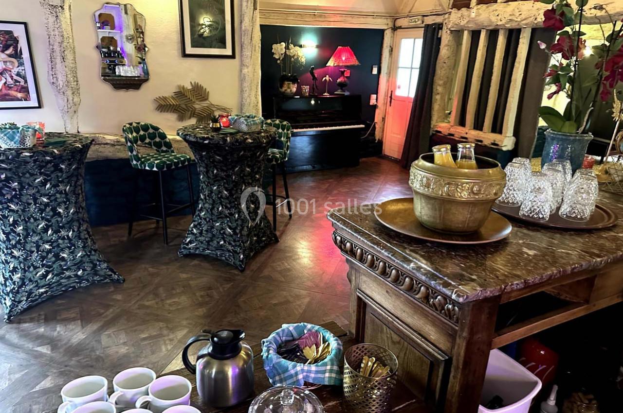 Salle décorée avec un bar en bois, tables hautes, piano en arrière-plan et ambiance chaleureuse.