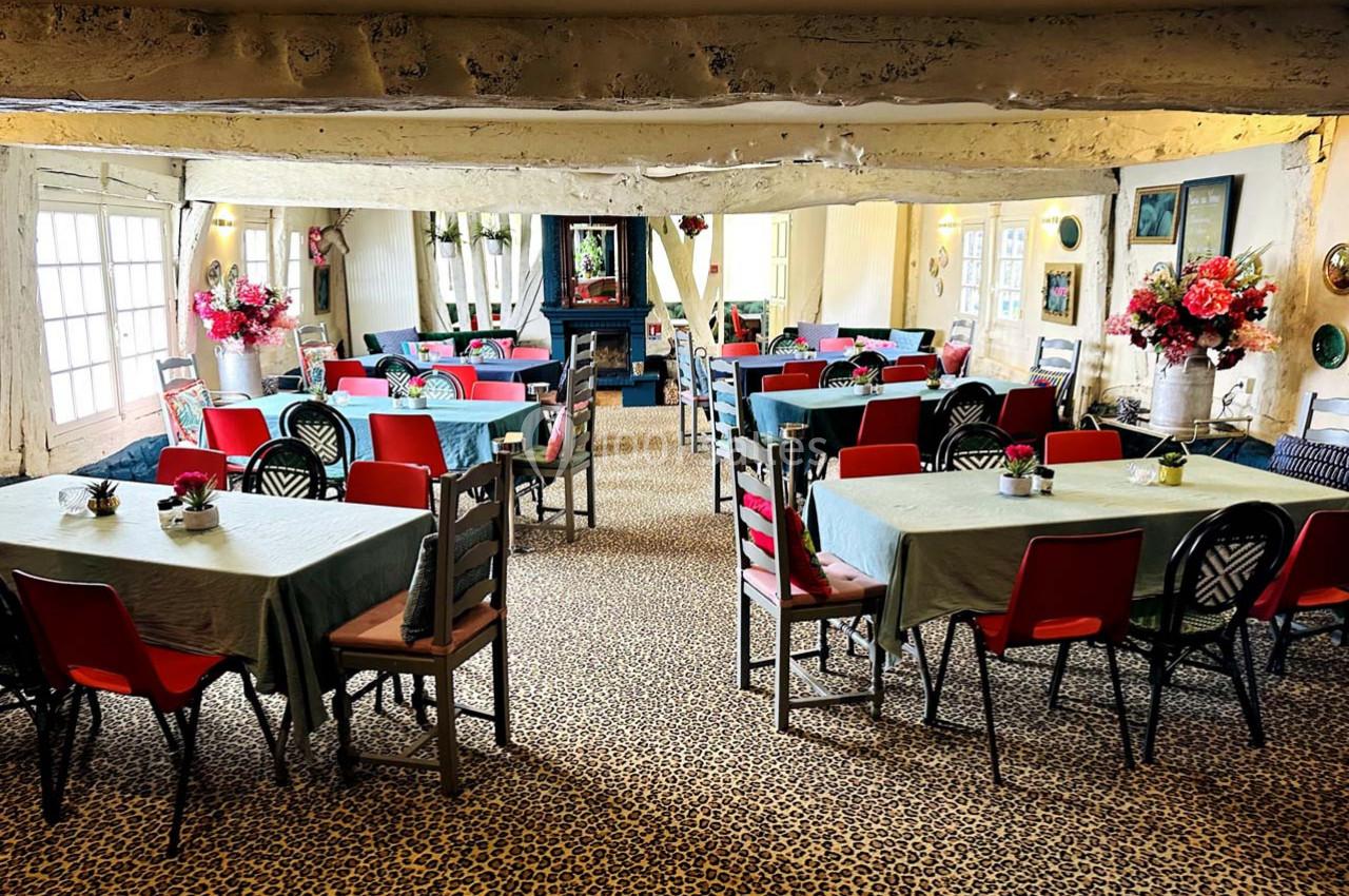 Salle de restaurant lumineuse avec tables dressées, chaises colorées et décorations florales sur un sol à motif léopard.