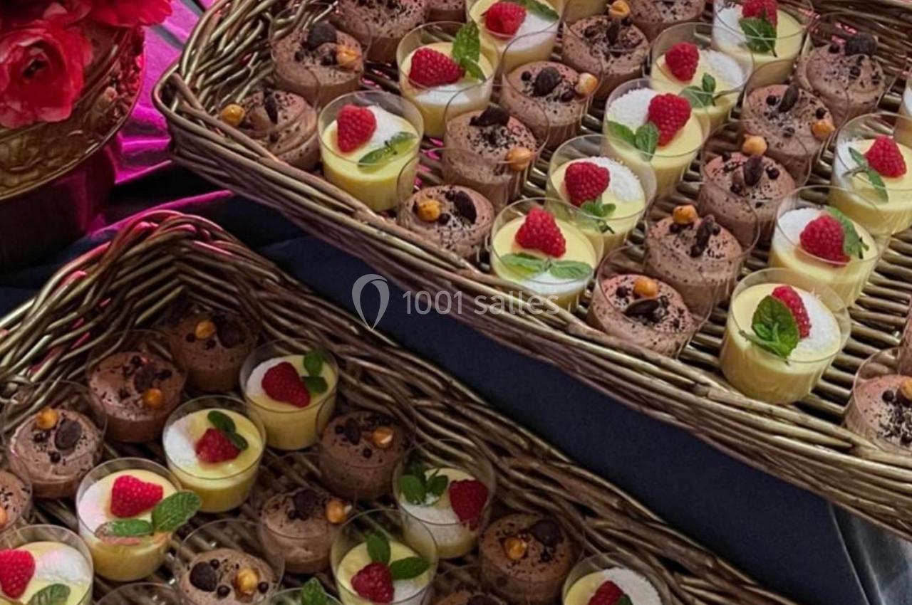 Plateaux en osier garnis de verrines de desserts variés, décorées de framboises, feuilles de menthe et autres garnitures.