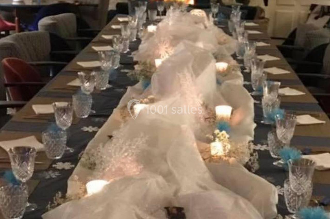 Table décorée pour un dîner, ornée de voiles blancs, bougies, fleurs et verres en cristal, dans une ambiance chaleureuse.