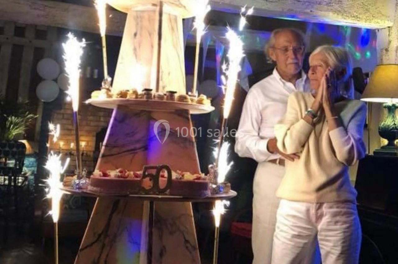 Un couple âgé célèbre un 50e anniversaire devant un grand gâteau décoré de bougies étincelantes.