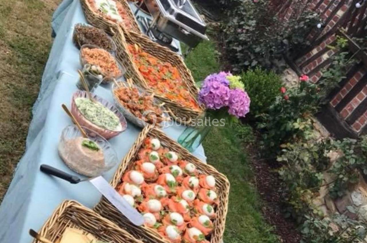 Buffet en extérieur avec plats variés présentés dans des paniers en osier, fleurs en décoration sur la table.