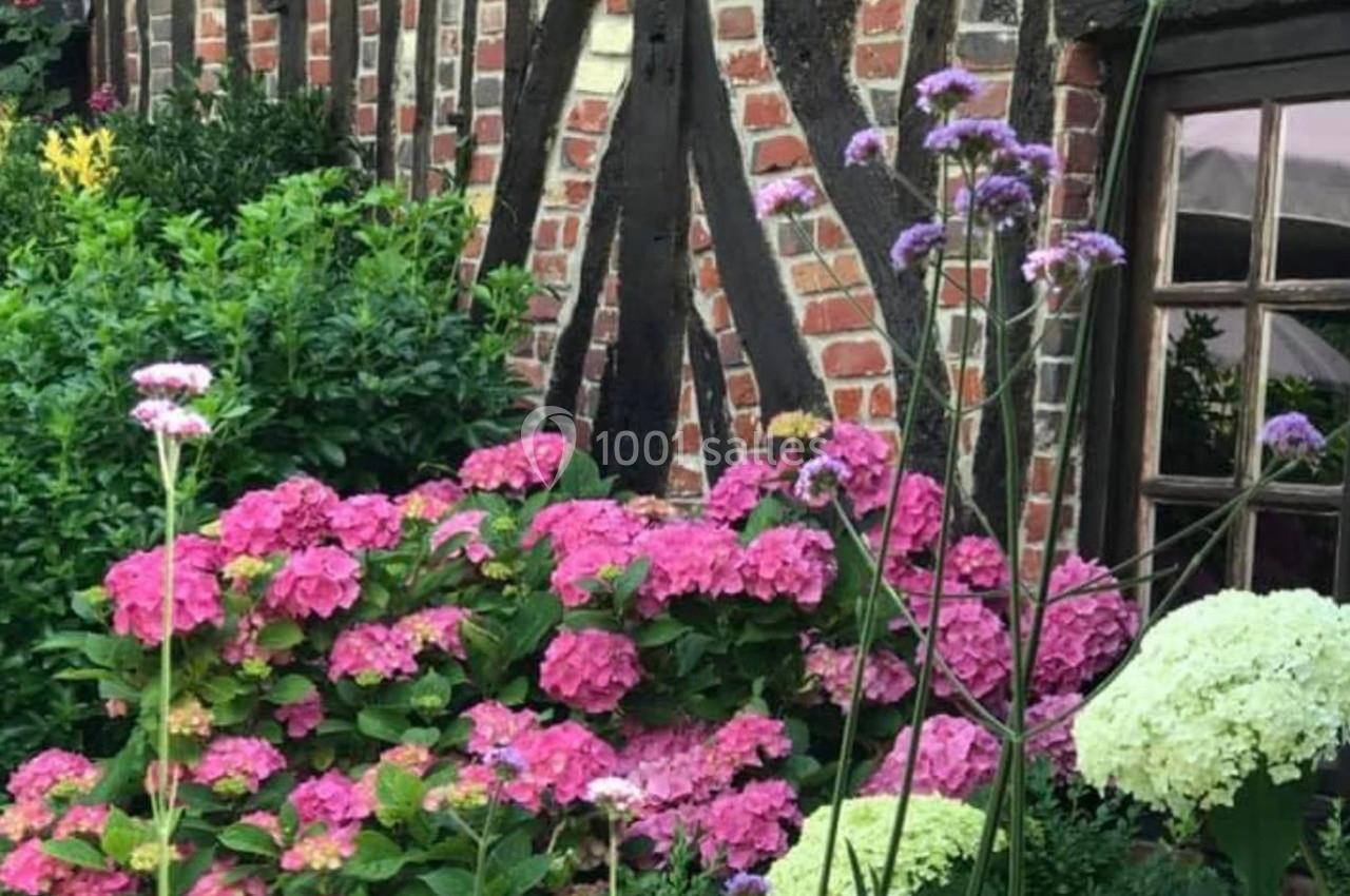 Façade en briques et bois d'une maison, entourée d'hortensias roses et blancs dans un jardin fleuri.